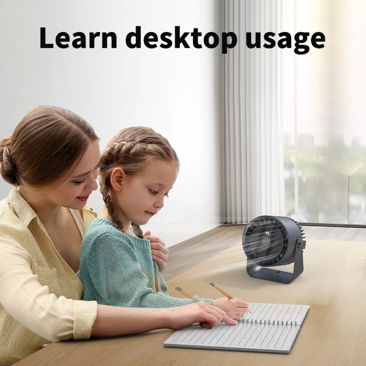 A mother and child are seated at a desk studying with a grey fan blowing air, and a notepad.