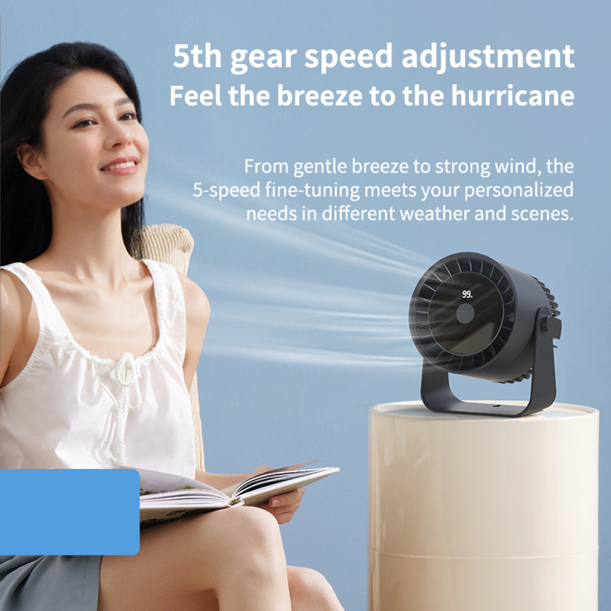 A woman sits near a fan, holding a book. The fan is black and the background is blue.