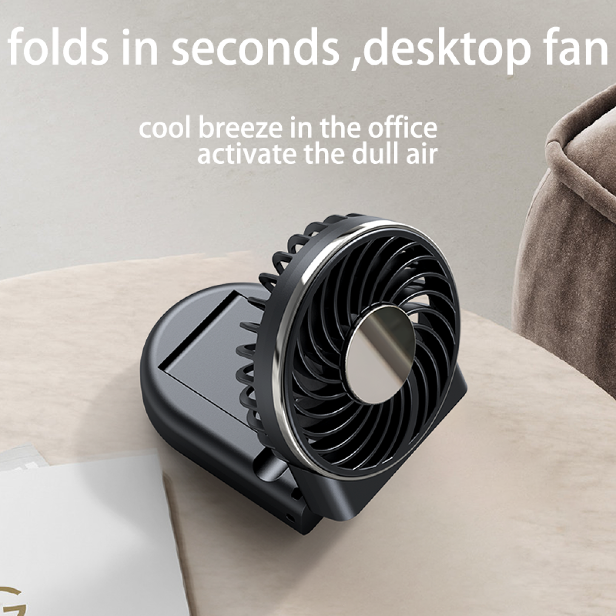 Black desktop fan, folded. It's on a desk with a white paper and a neutral background.