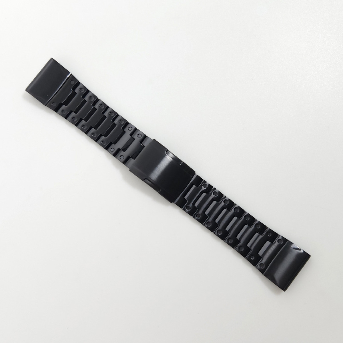 Ein schwarzes Uhrenarmband mit Gliedern. Das Armband liegt auf einer weißen Oberfläche.