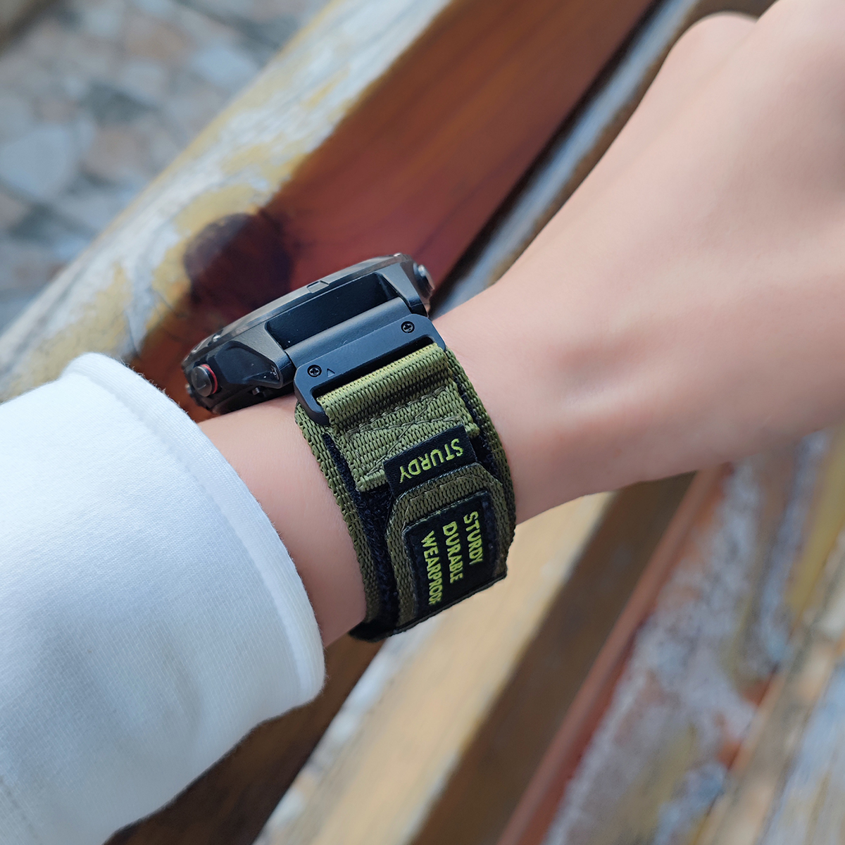 Das Handgelenk einer Person mit einer schwarzen Uhr und einem grün-schwarzen Armband mit der Aufschrift "STURDY DURABLE WEARPROOF".