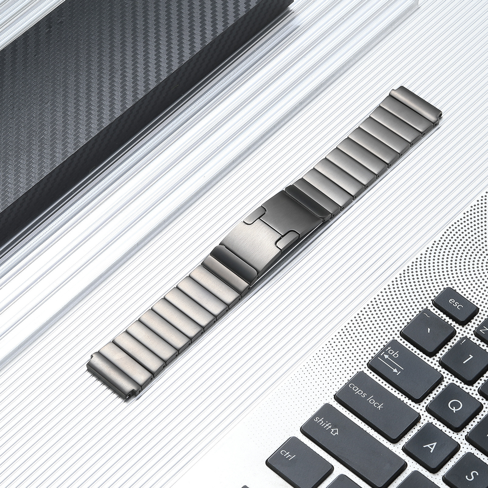 Ein Metall-Uhrenarmband auf einer Laptop-Tastatur. Das Armband ist grau mit einem Verschluss. Die Tastatur ist grau.