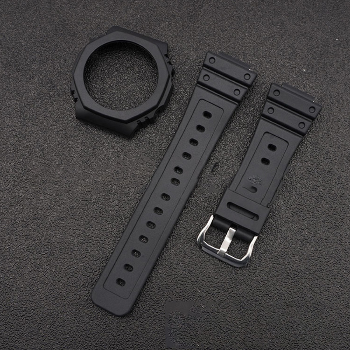 Schwarze Uhrenkomponenten, einschließlich Lünette und Armbänder, auf dunkler Oberfläche angeordnet.