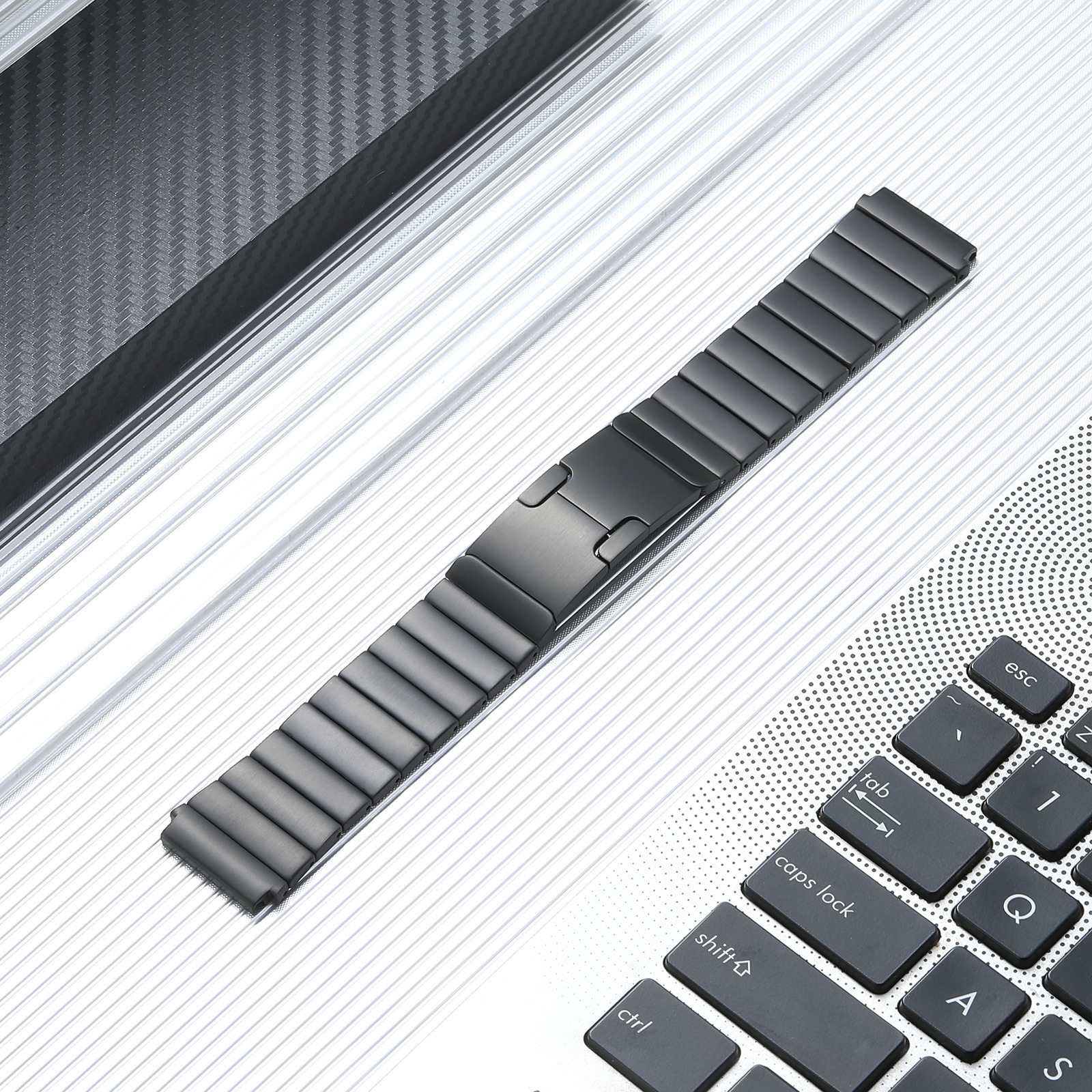 Schwarzes Metall-Uhrenarmband mit Verschluss, das auf einer hellen Oberfläche mit Tastatur liegt.