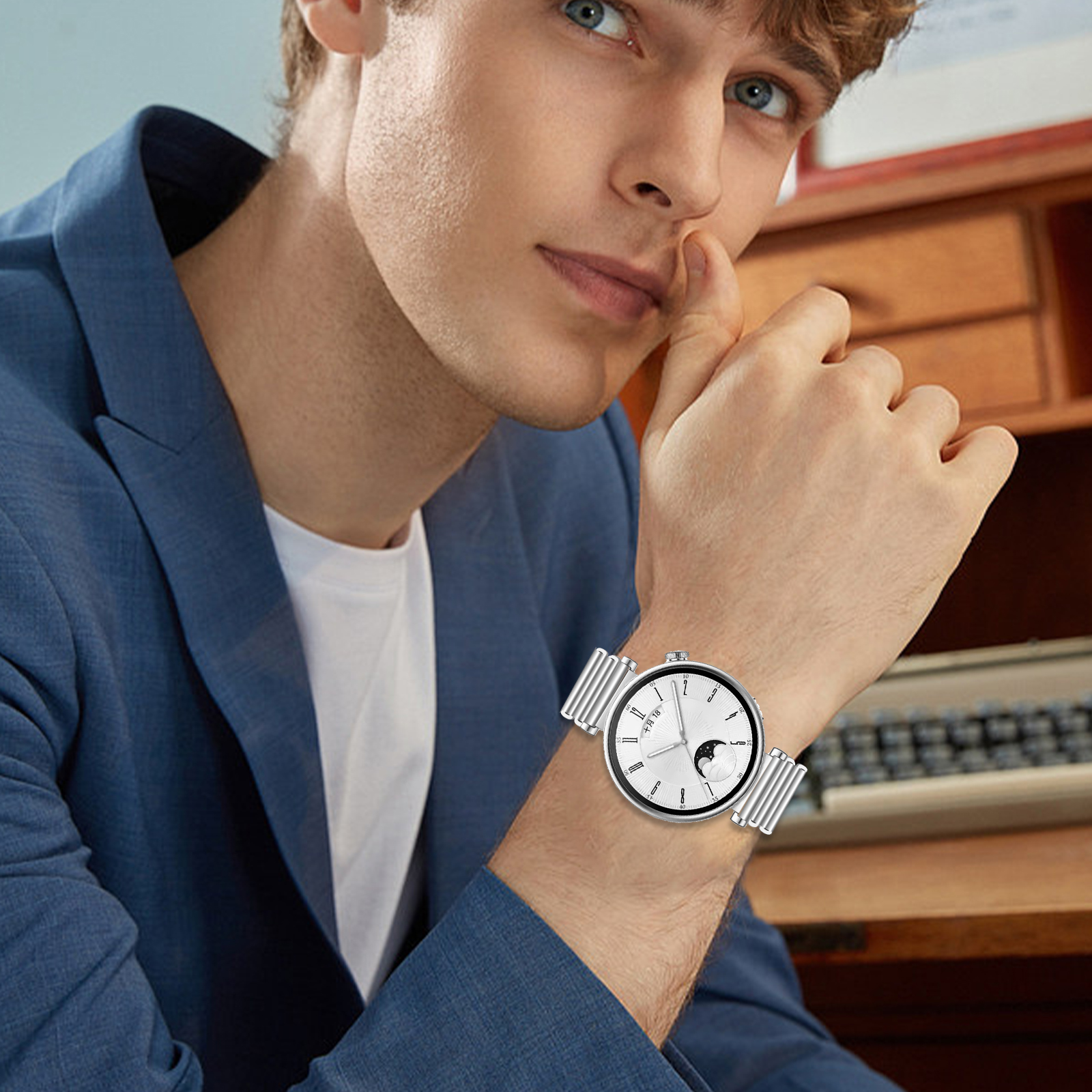 Uomo con orologio con quadrante bianco e cinturino in metallo. Indossa un blazer blu.