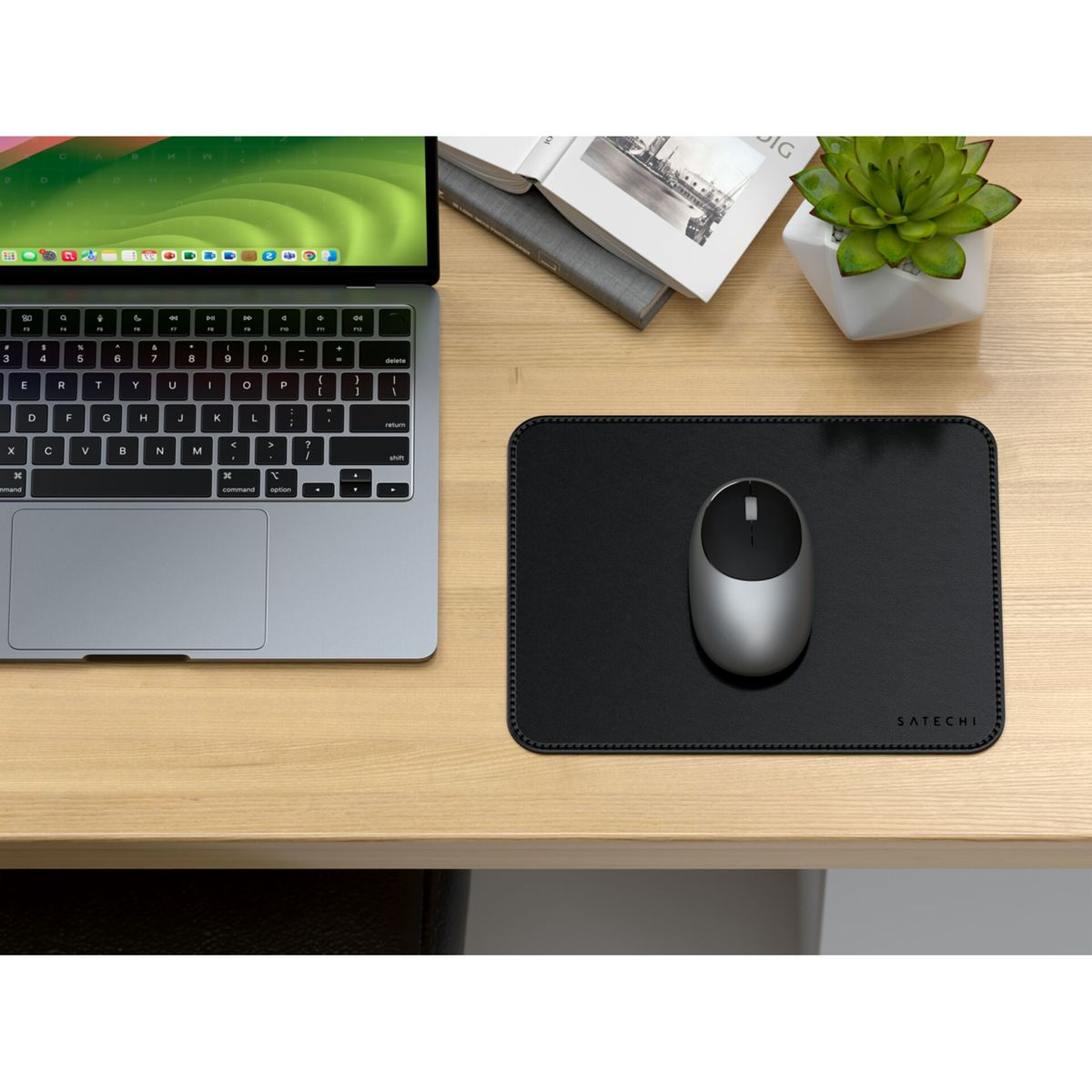 Ein Laptop, eine Maus, ein Mauspad und eine Pflanze auf einem Holzschreibtisch. Das Mauspad ist schwarz, die Maus silbern.