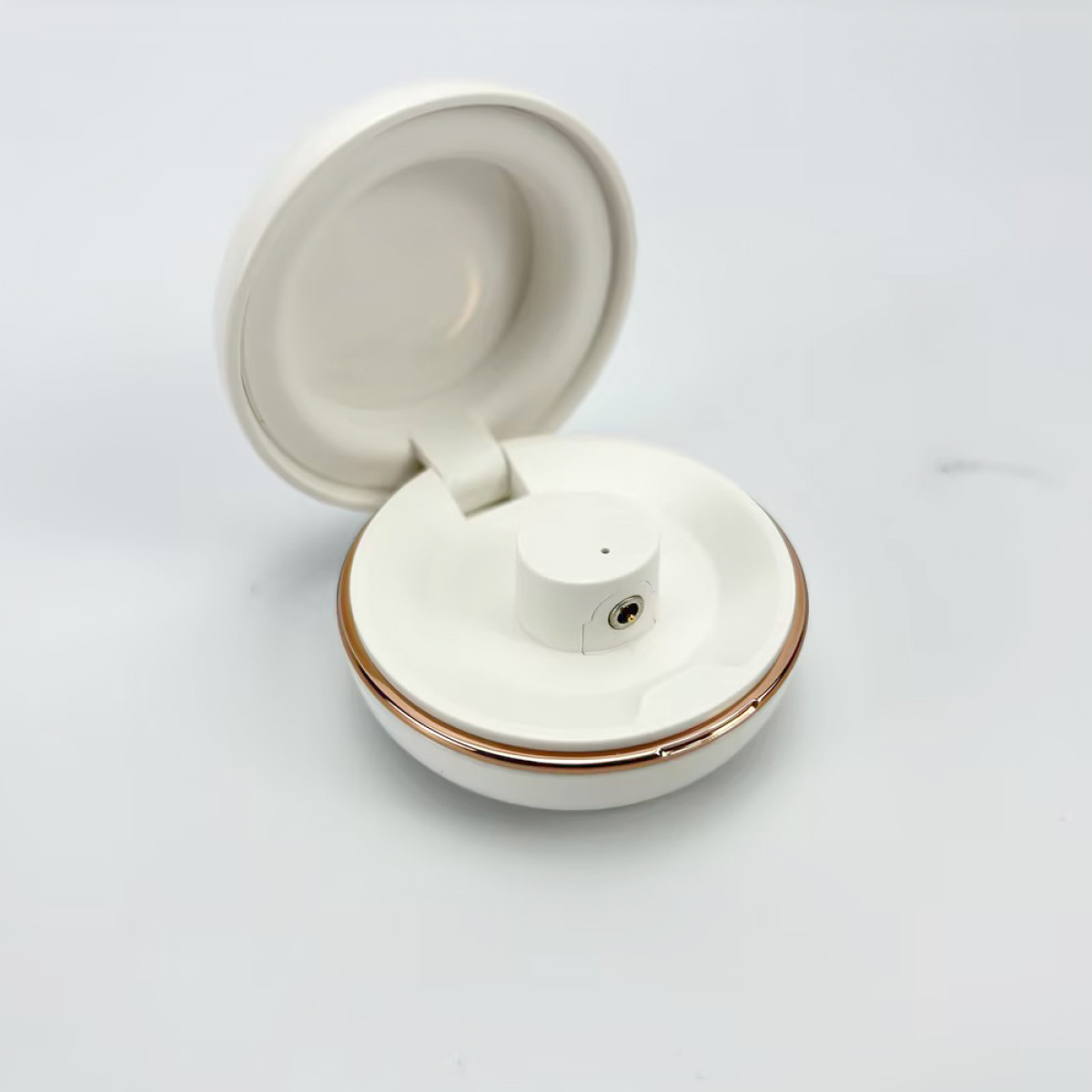 Białe, otwarte, okrągłe etui na słuchawki z jednym wkładem dousznym w środku.