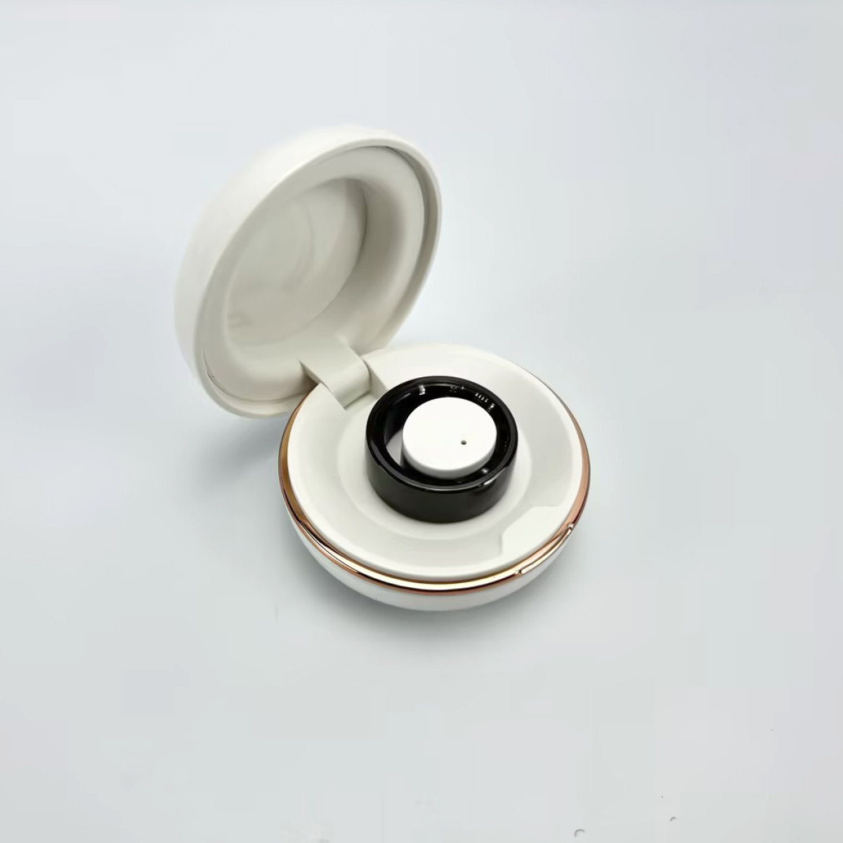 Otwarta biała obudowa ładująca, odsłania czarną podkładkę ładującą w białej, okrągłej podstawie ze złotym wykończeniem.