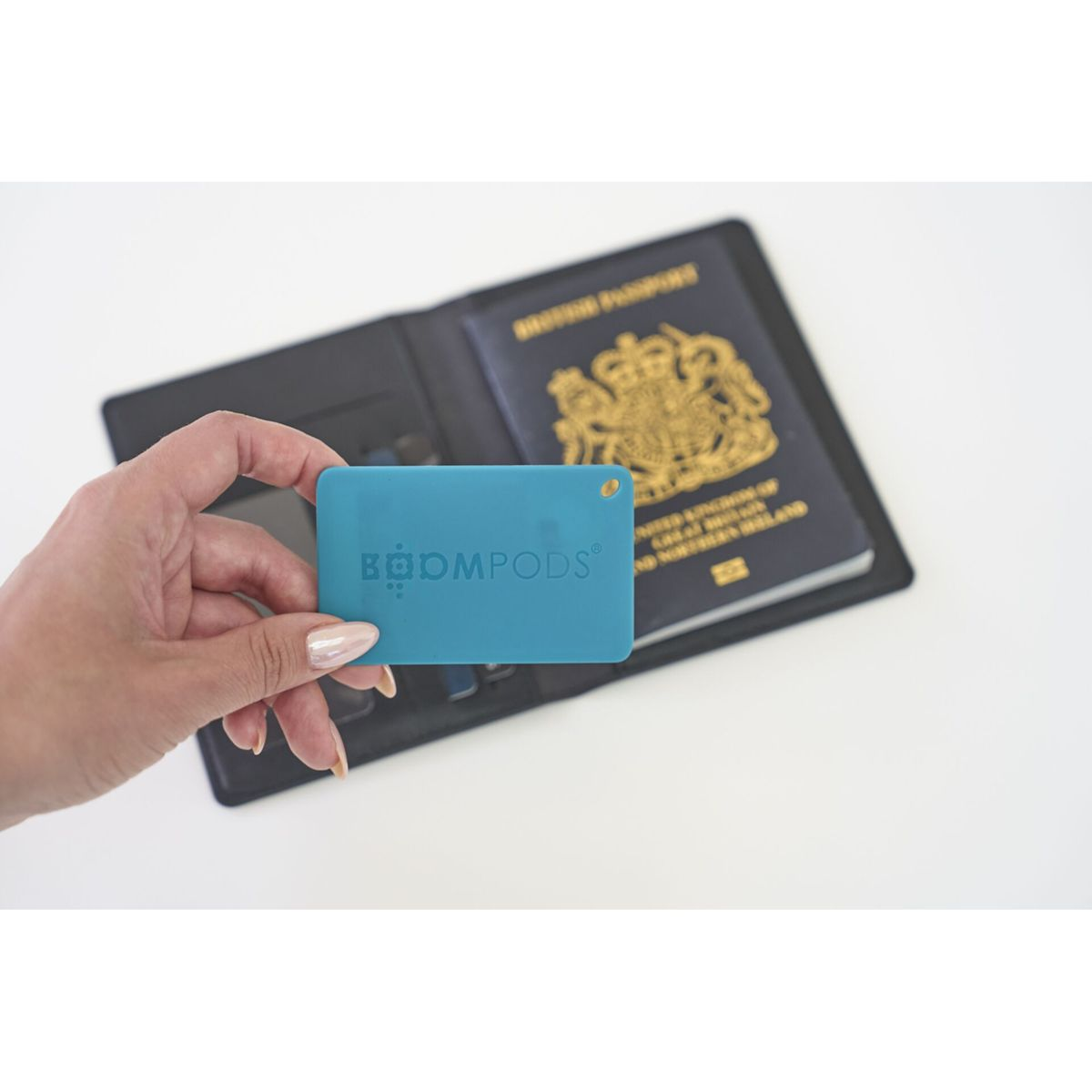 Kobieta trzymająca niebieską kartę Boompods i otwarty paszport. Czarne skórzane etui w tle.