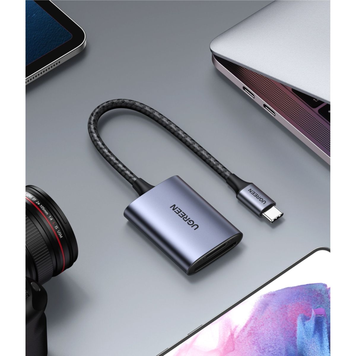 Silberner und grauer USB-C-Hub mit Kabel. UGREEN-Text. Laptop und Tablet im Hintergrund.
