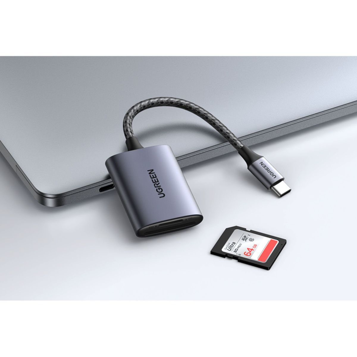 Ein silberner UGREEN-Adapter mit USB-C-Kabel und einer SD-Karte, platziert auf einem Laptop.