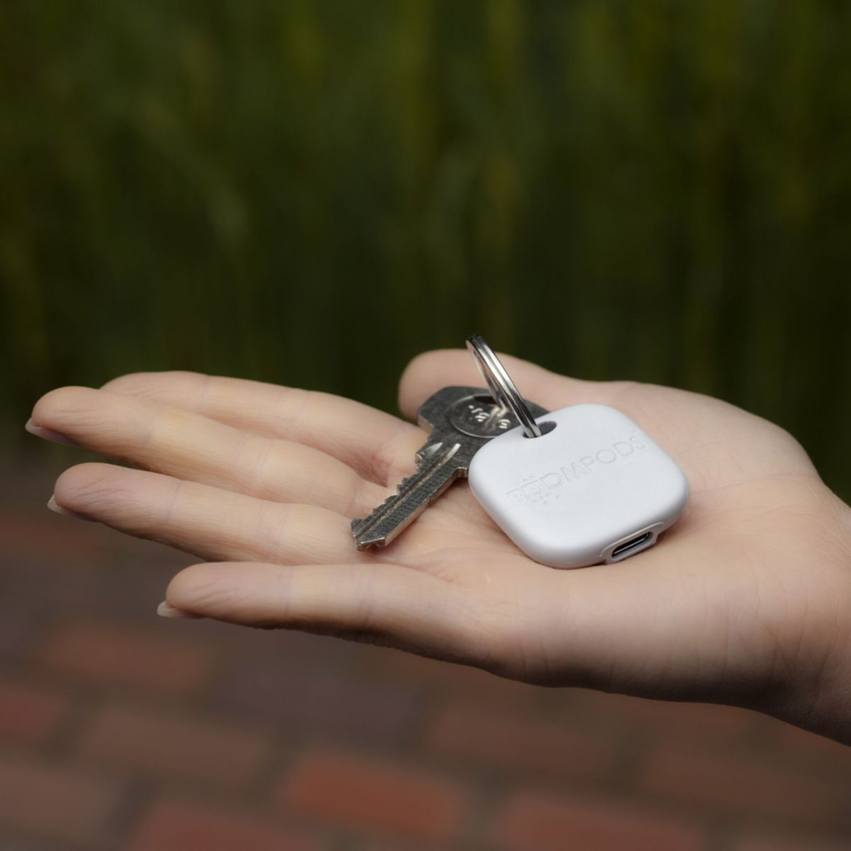 Mano che tiene chiavi e un localizzatore di chiavi bianco con una porta di ricarica.