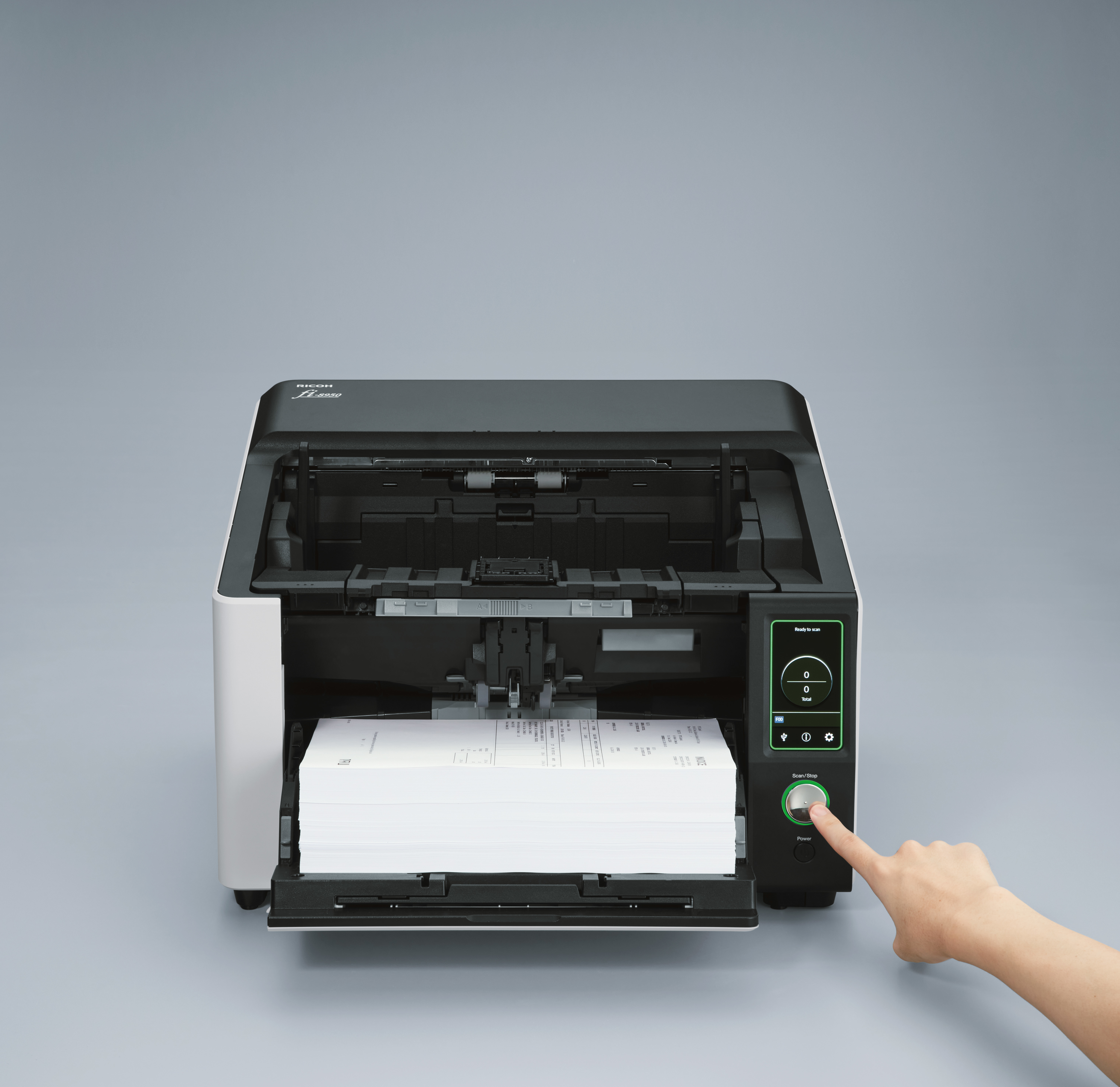 Een grote zwart-wit scanner met een stapel papier erin. Een hand drukt op de startknop.