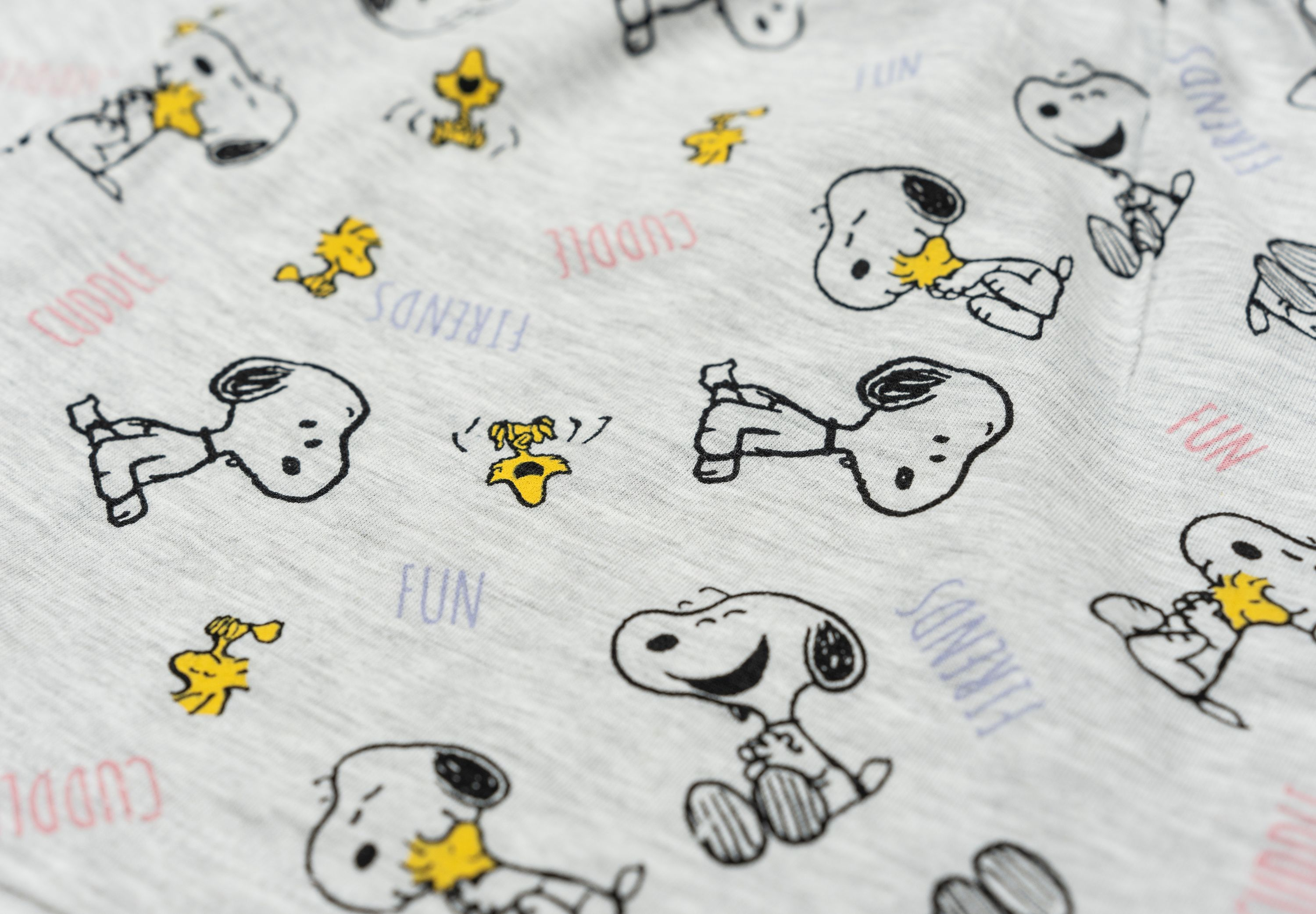 Nahaufnahme des Snoopy-Musters auf grauem Stoff. Snoopy-Posen, Wörter und andere Details sind sichtbar.