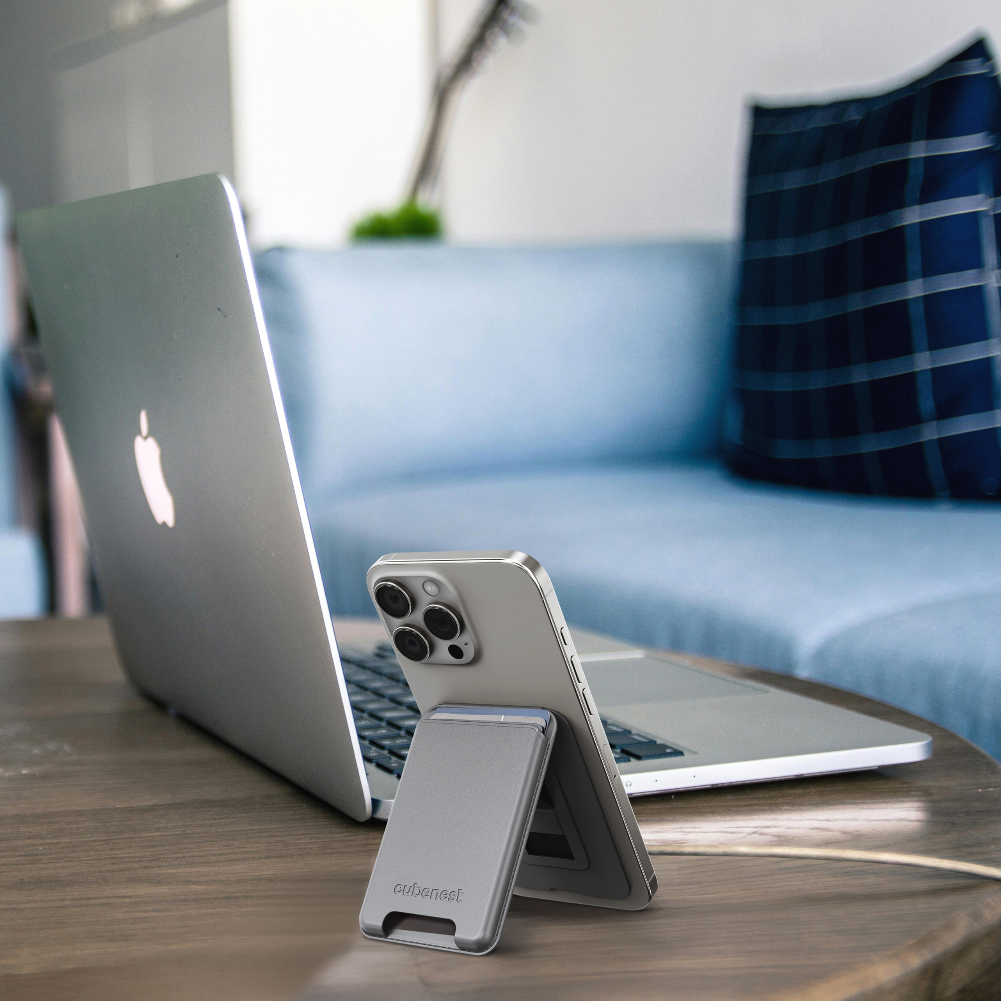 Ein Laptop und ein Telefonständer auf einem Holztisch, im Hintergrund eine blaue Couch.