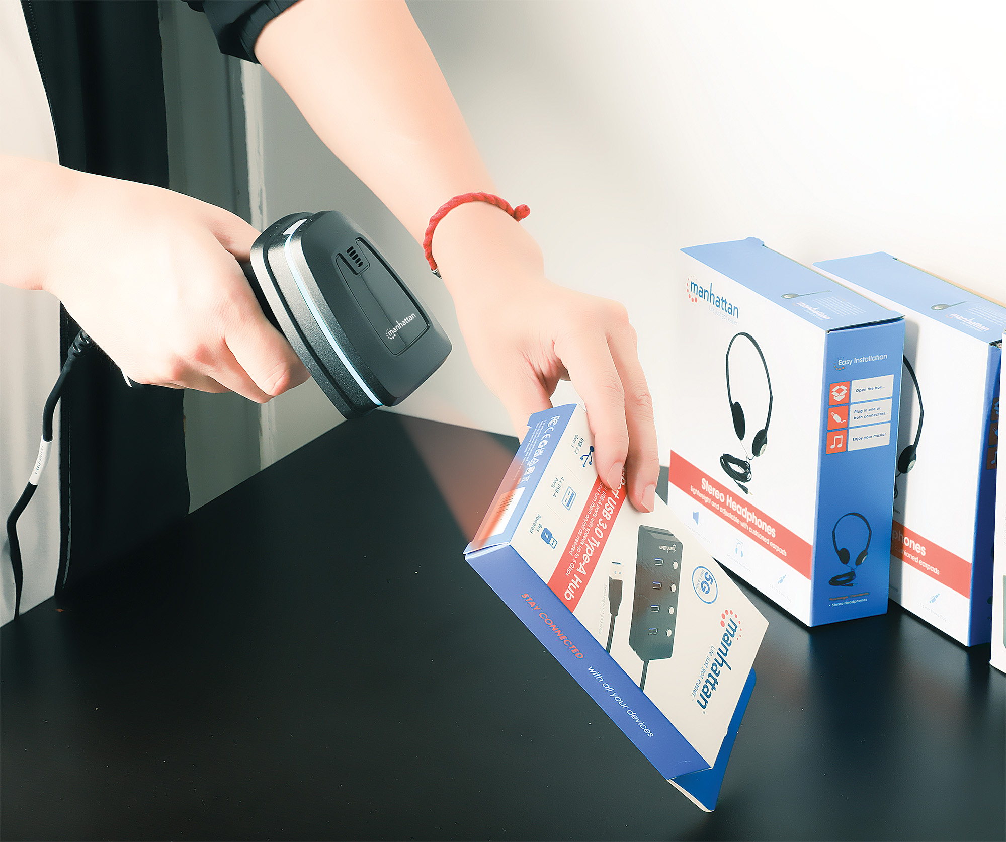 Una persona scansiona una scatola con uno scanner di codici a barre. Altre scatole visibili.