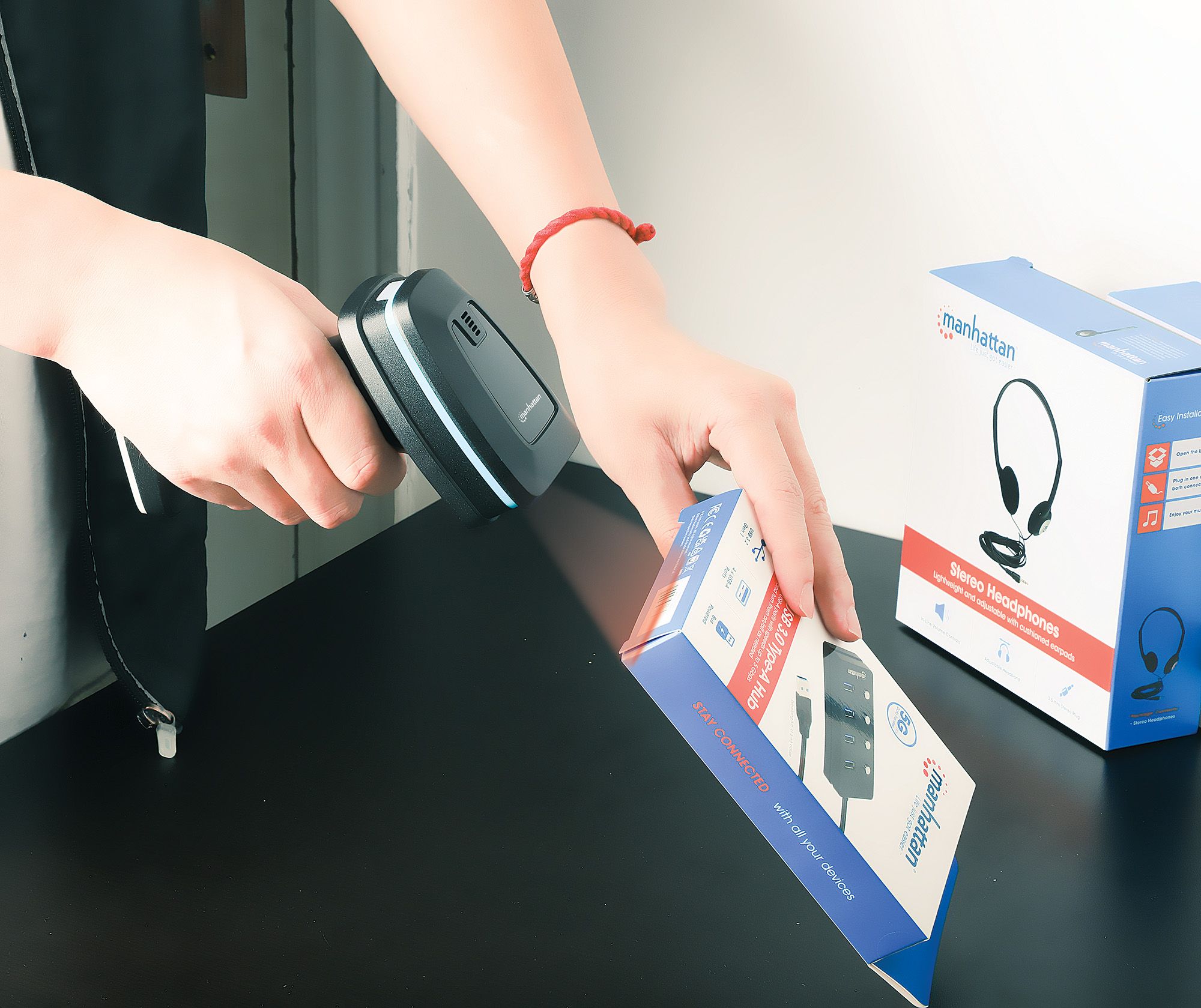 Mani che usano uno scanner di codici a barre per scansionare una scatola. Scatole e scrivania visibili.