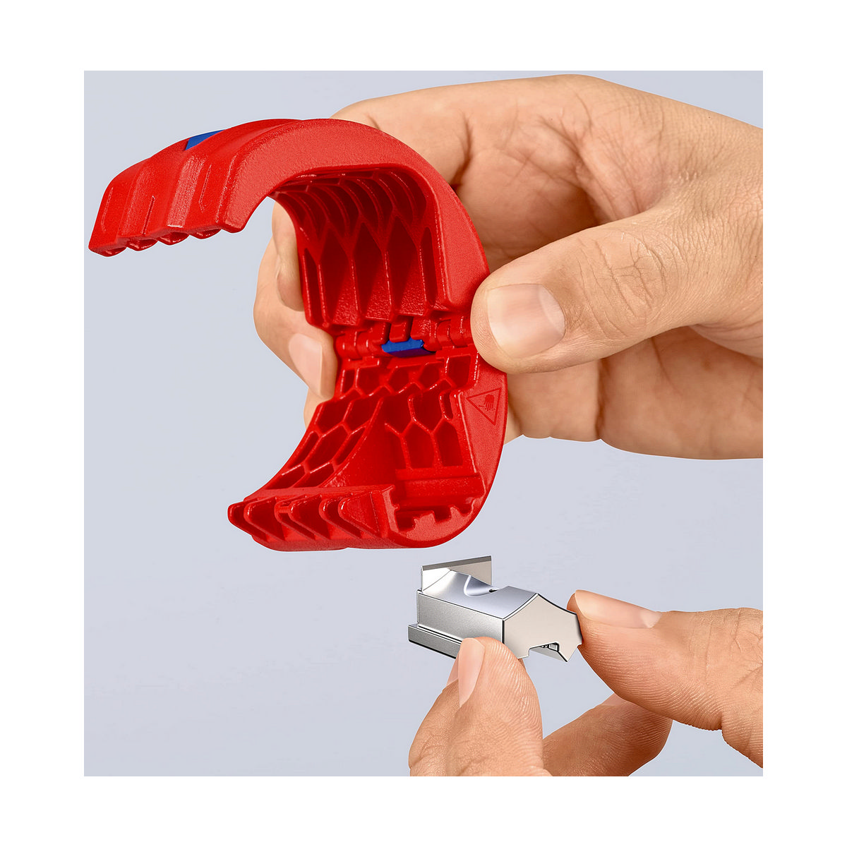 A hand is holding a blade and a red pipe cutter. The blade is silver, and the tool has a blue accent.