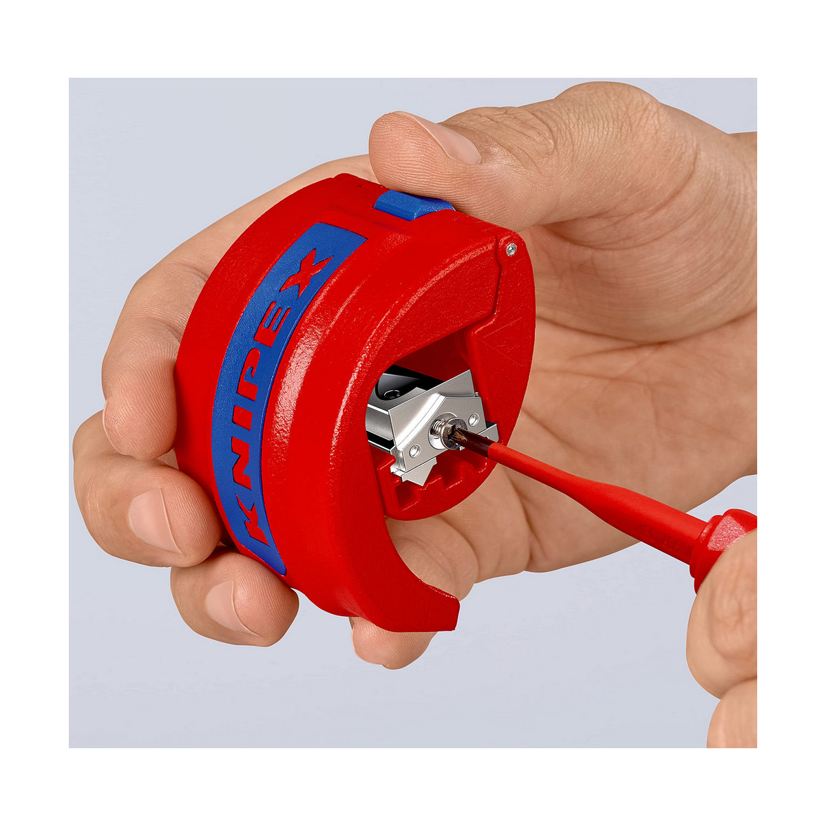 Hand holding a red and blue Knipex pipe cutter, with a screwdriver inside.