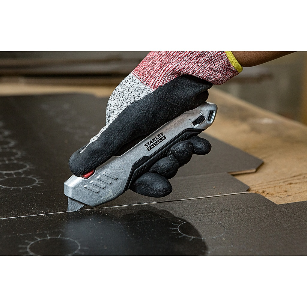 Hand im Handschuh schneidet mit einem silbernen Universalmesser eine schwarze Oberfläche.
