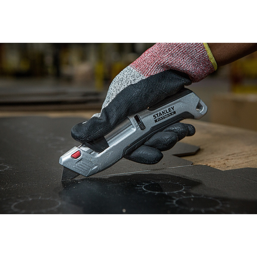 Eine Hand mit Handschuh schneidet mit einem silbernen Universalmesser eine dunkle Oberfläche.