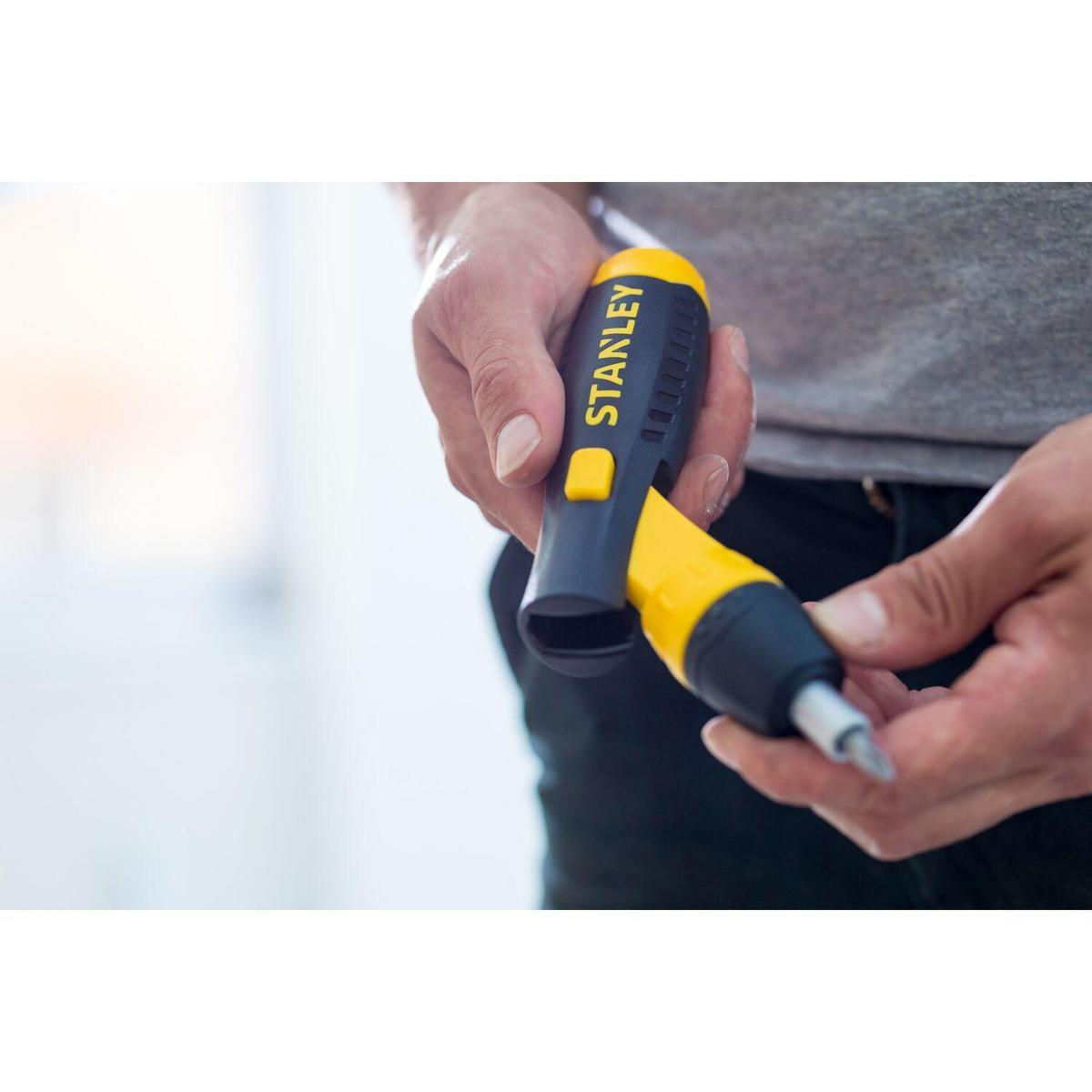 Osoba trzymająca śrubokręt Stanley. Żółto-czarny uchwyt. Białe tło.