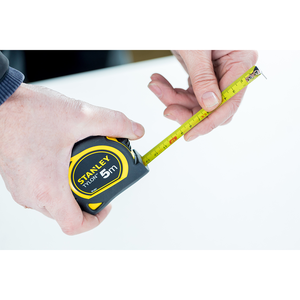Osoba używająca miarki Stanley. Czarno-żółta obudowa. Biała powierzchnia.