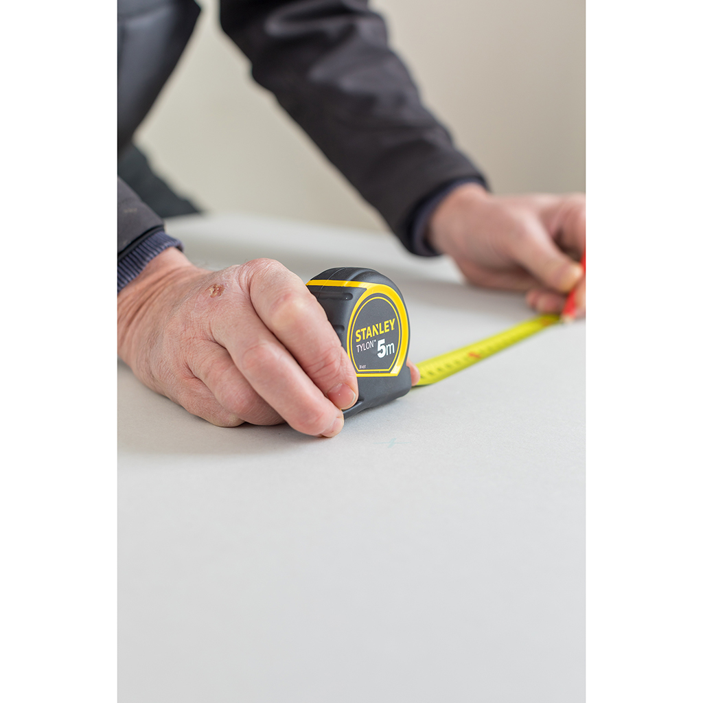 Osoba używająca miarki Stanley. Czarno-żółta obudowa, pomiar na powierzchni.