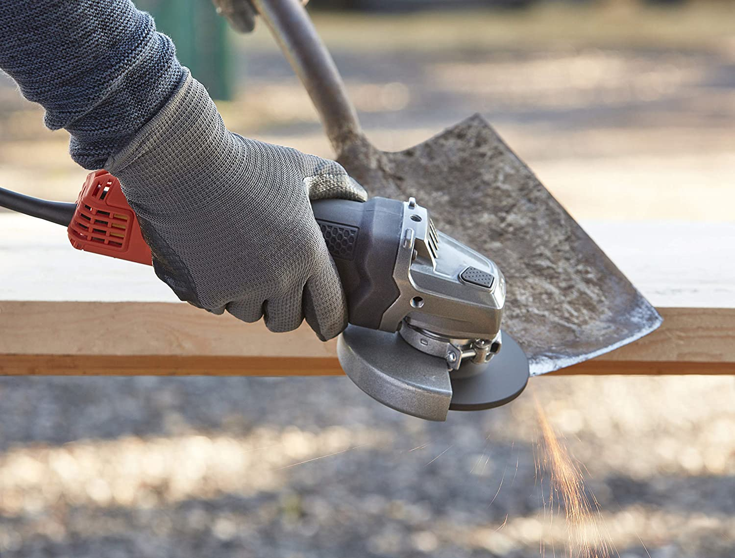 Persoon die een haakse slijper op hout gebruikt, er zijn vonken aanwezig. De tool staat in de buurt van een schop.