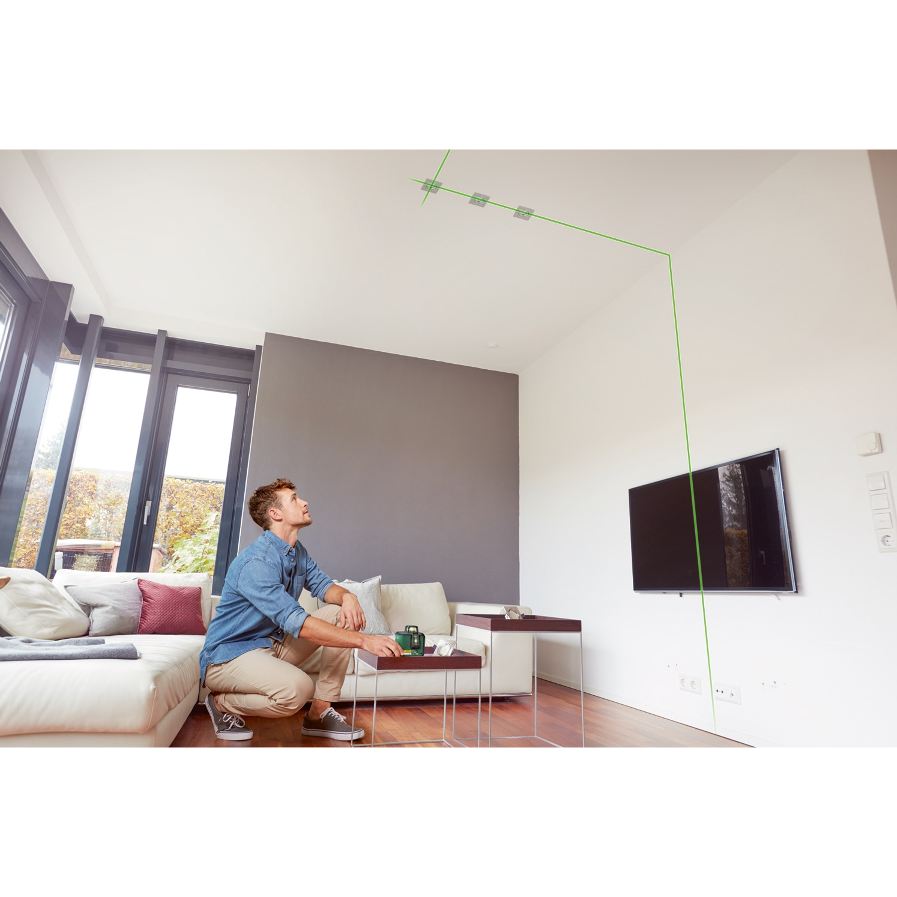 Mężczyzna patrzący na poziomicę laserową na suficie, w salonie.