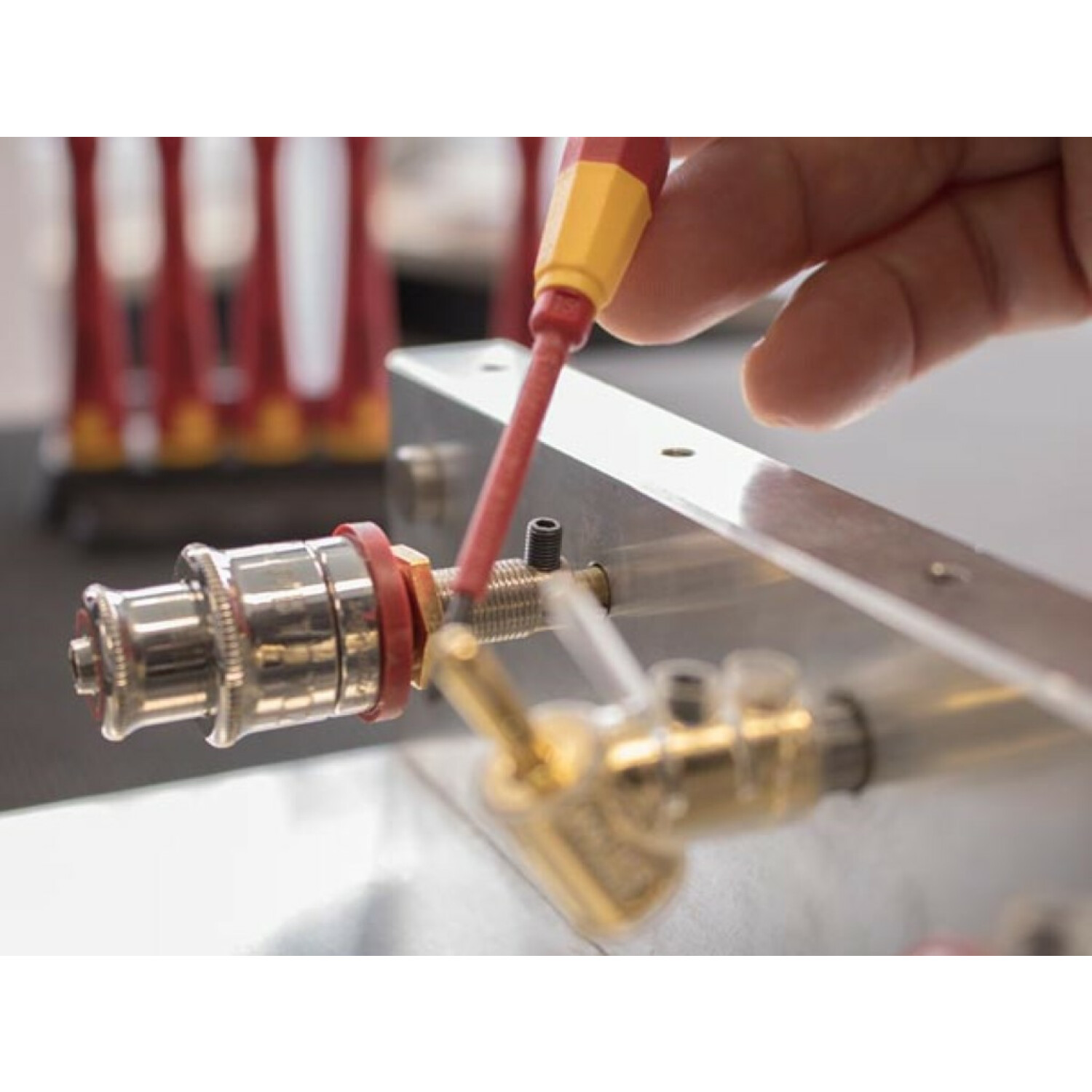 Osoba używająca czerwono-żółtego śrubokręta na metalowej części.