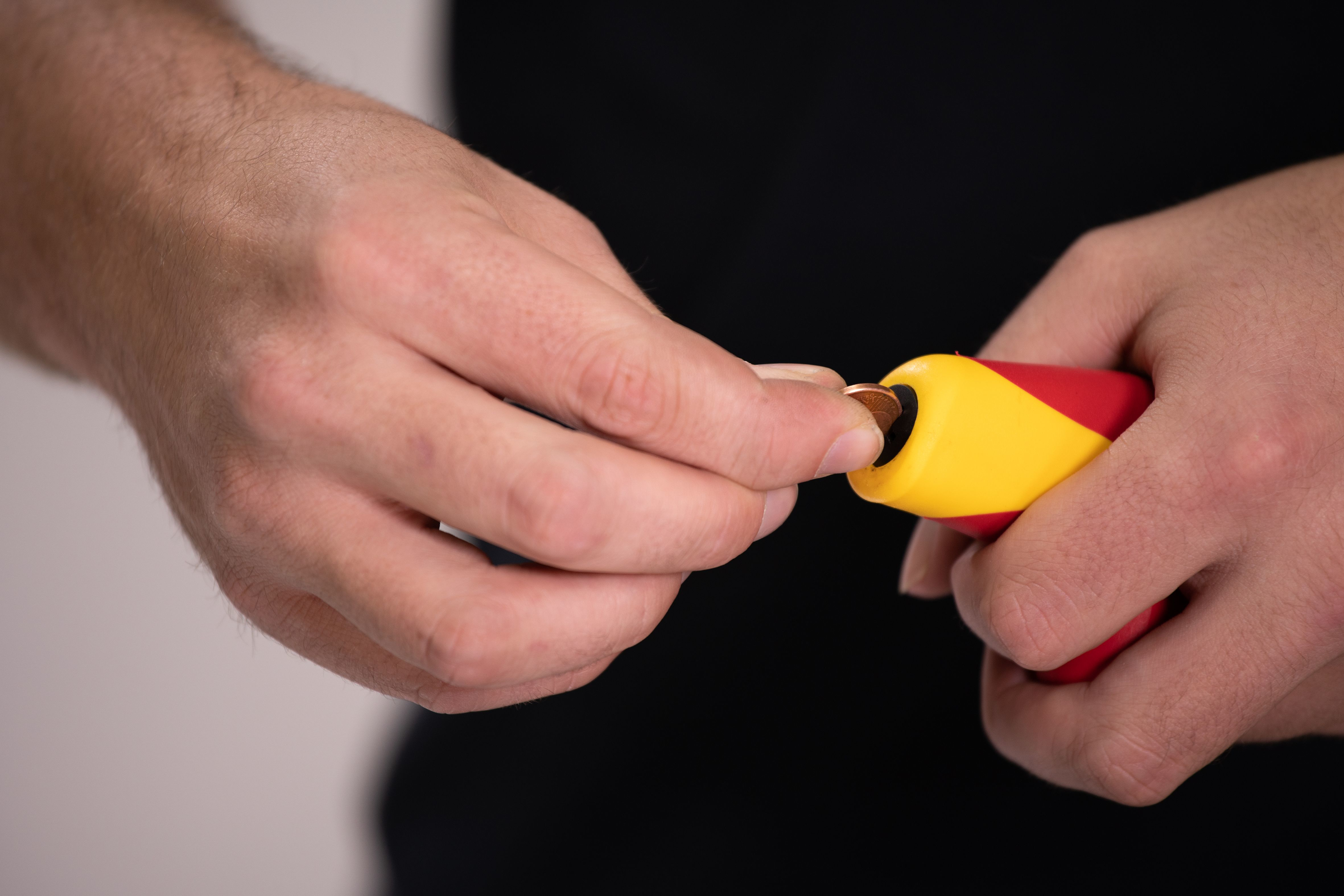 Mani che inseriscono una moneta nella fessura di uno strumento rosso e giallo, primo piano.