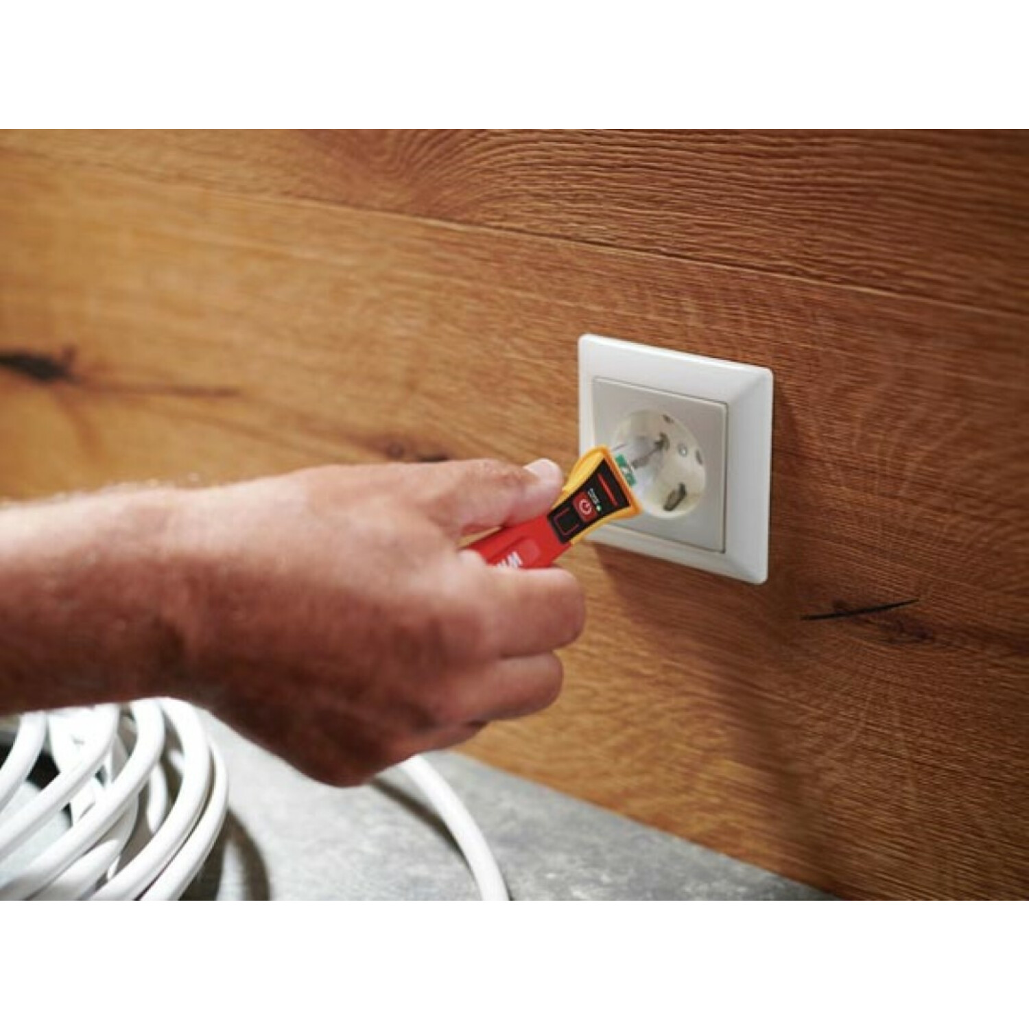Ręka wkłada czerwono-żółty tester napięcia Wiha do białego gniazdka ściennego.