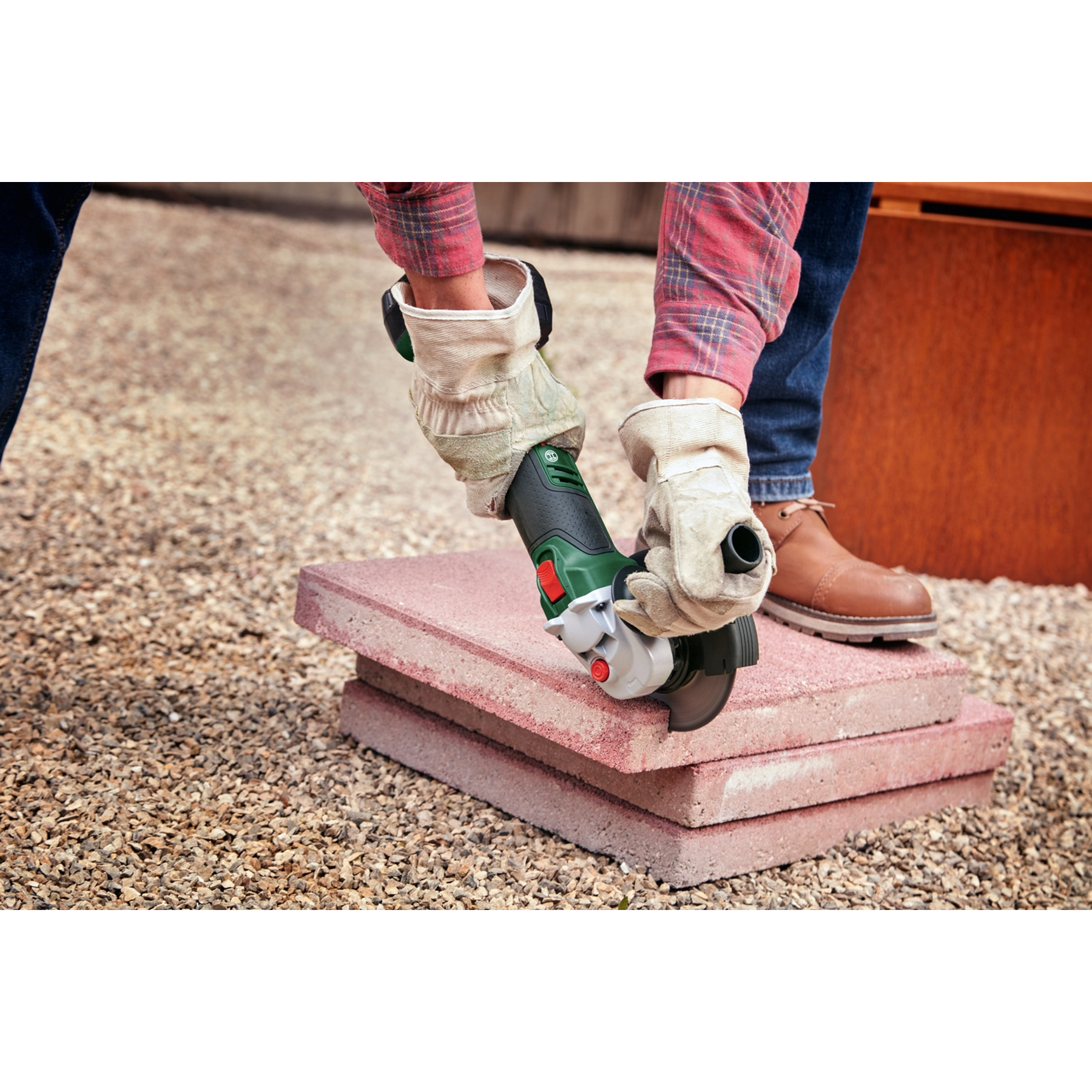 Osoba używająca szlifierki kątowej do cięcia różowych cegieł. Ma na sobie rękawice i okulary ochronne.