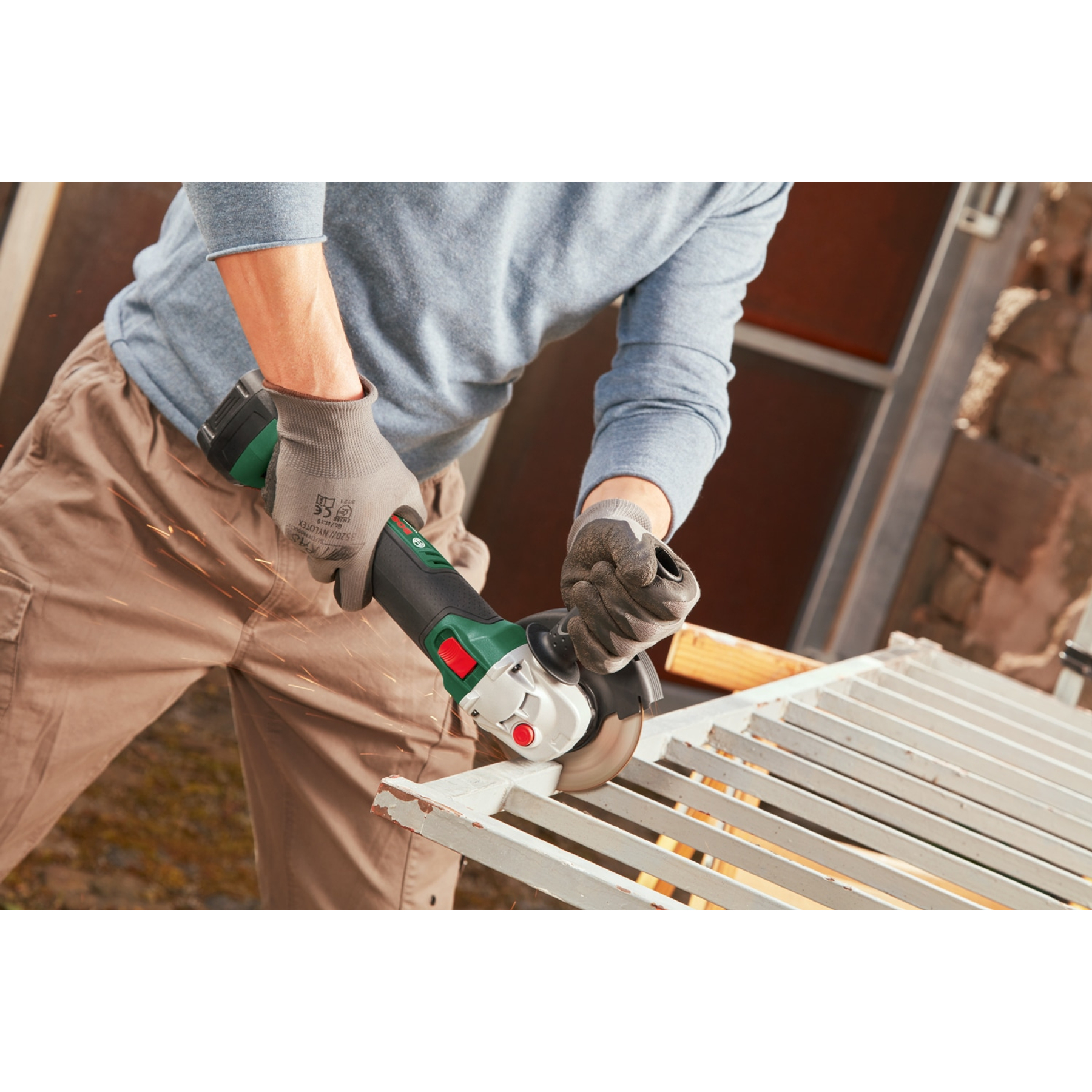 Mężczyzna używa szlifierki na metalowej bramie. Iskry lecą. Tło obejmuje budynek i niebo.