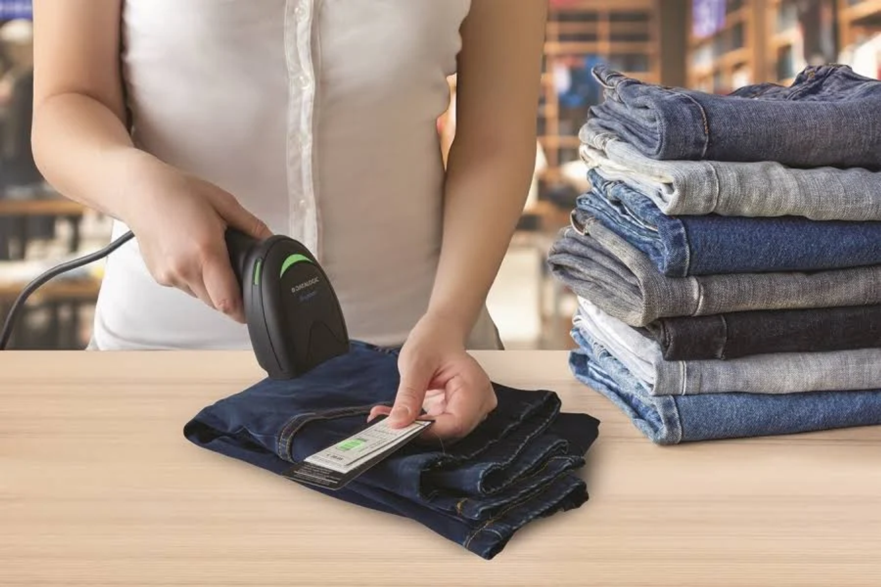Una persona che scansiona un'etichetta su un paio di jeans. Una pila di jeans è sulla destra.