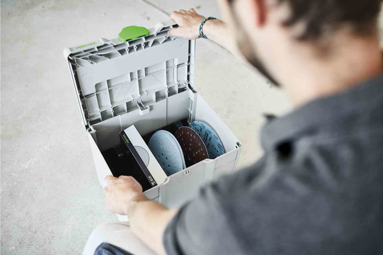 Osoba otwiera skrzynkę narzędziową Festool, ukazując tarcze szlifierskie i inne.