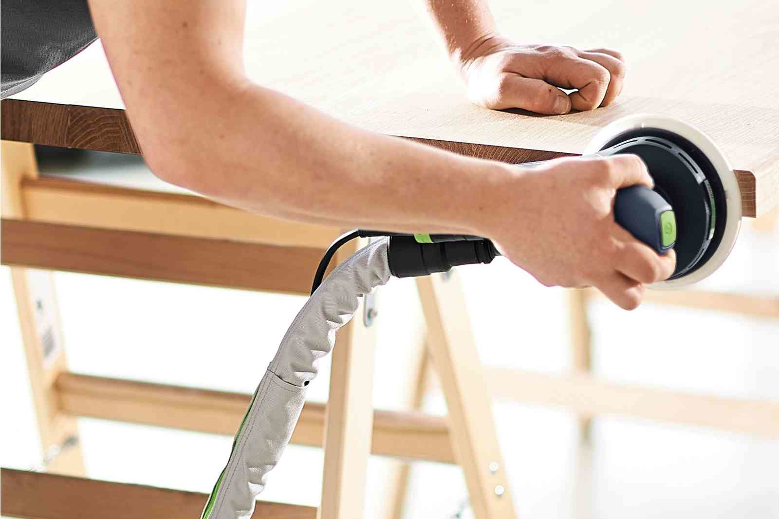 Osoba szlifuje drewnianą powierzchnię szlifierką elektryczną. Szlifierka i drewno są brązowe.