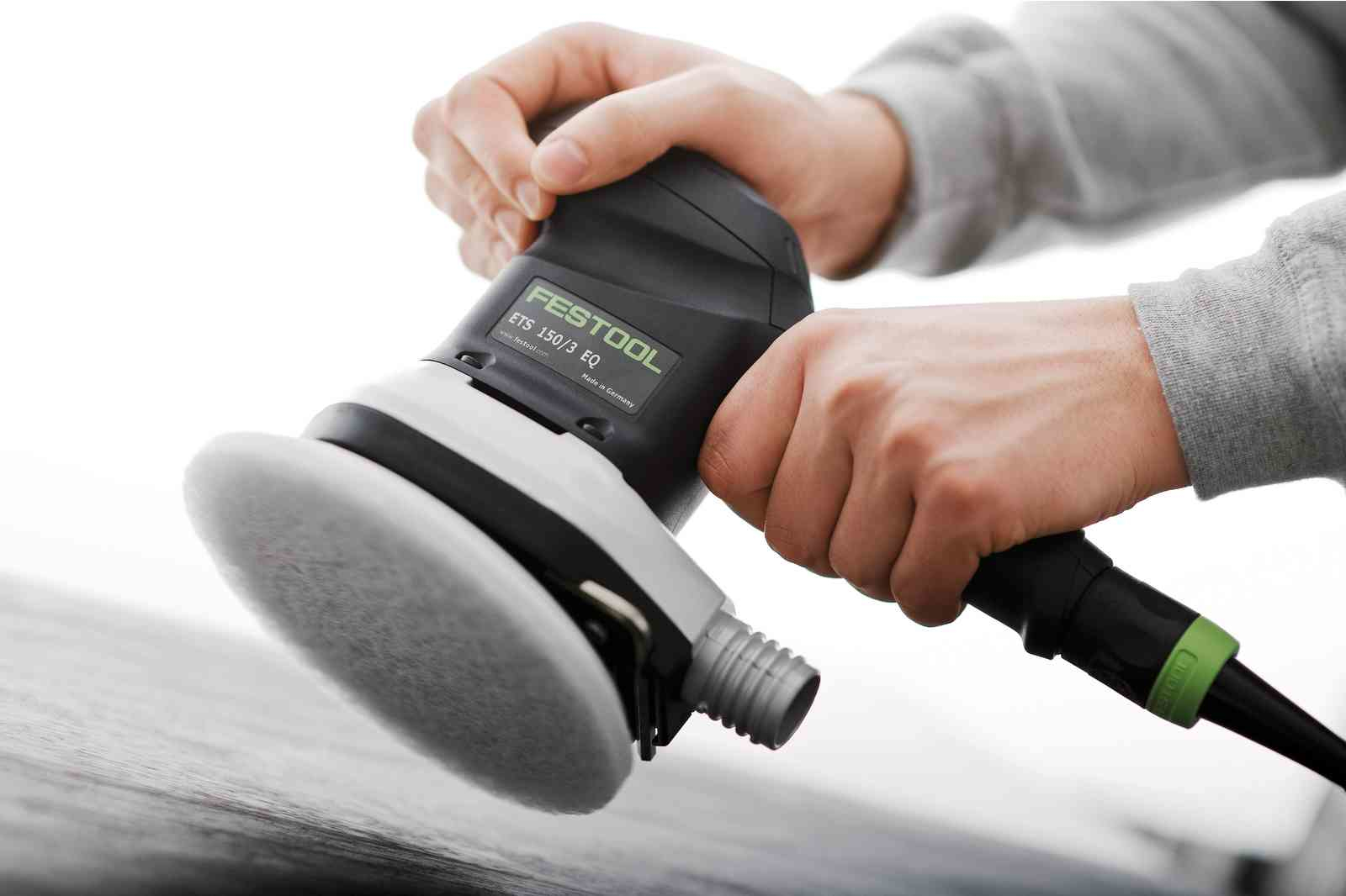 Zbliżenie osoby trzymającej czarno-białą szlifierkę elektryczną. Szlifierka jest w użyciu.