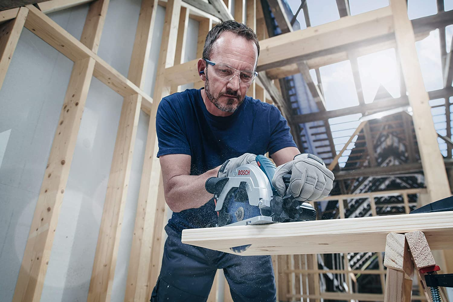 Mann mit Schutzbrille und Gehörschutz, schneidet Holz mit einer Kreissäge.