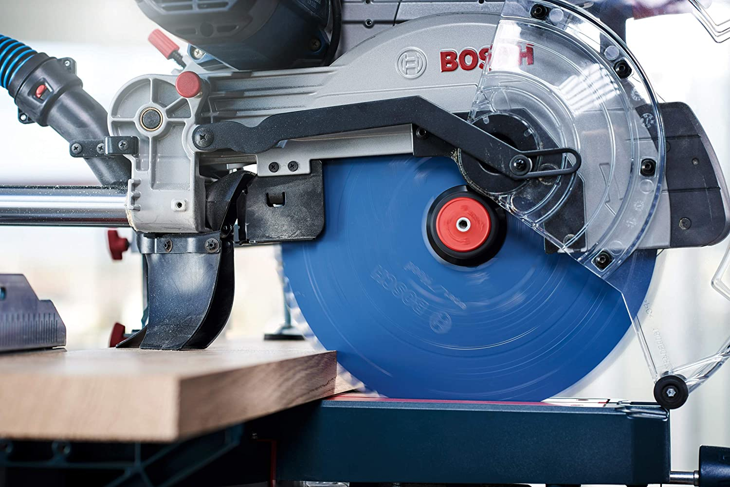 Bosch-Gehrungssäge schneidet Holz. Sägeblatt ist blau. Holz liegt auf dem Sägetisch.
