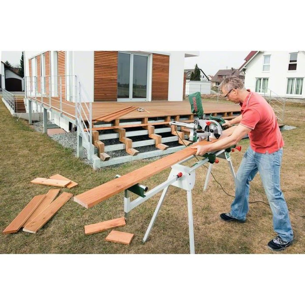Mann im roten Hemd benutzt eine Gehrungssäge, um Holz im Freien am Haus zu schneiden.