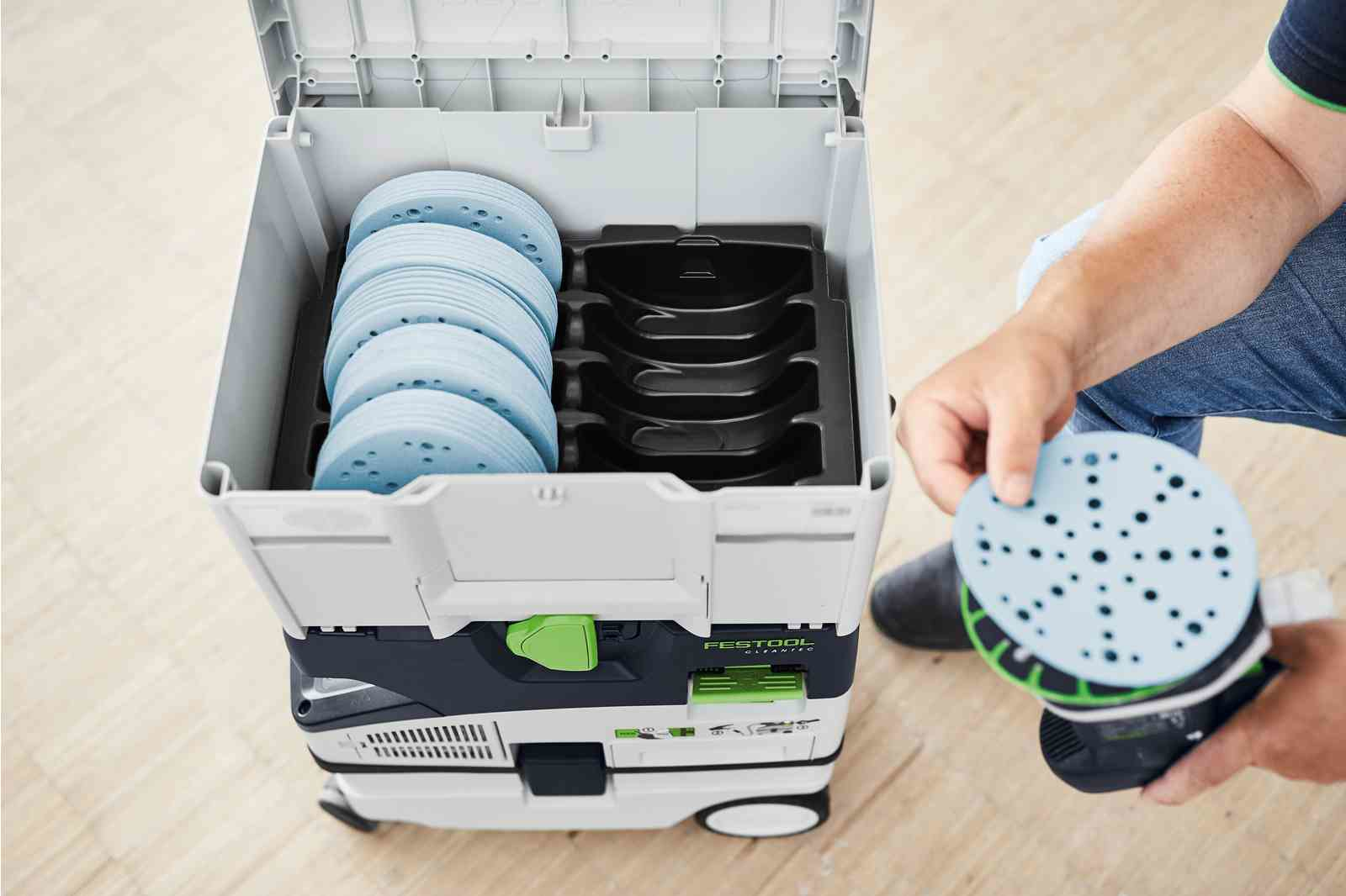 Ręka trzymająca tarczę szlifierską obok otwartej skrzynki narzędziowej z tarczami szlifierskimi.