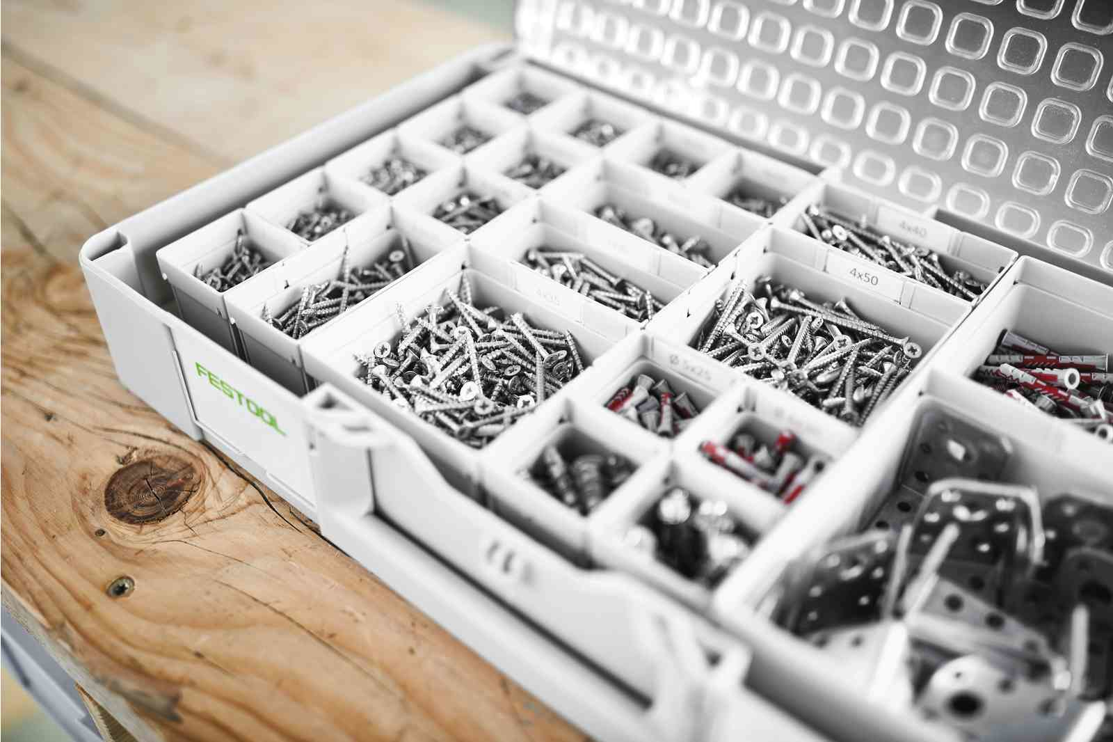 Otwarta, biała skrzynka narzędziowa, wypełniona śrubami i mocowaniami na drewnie.