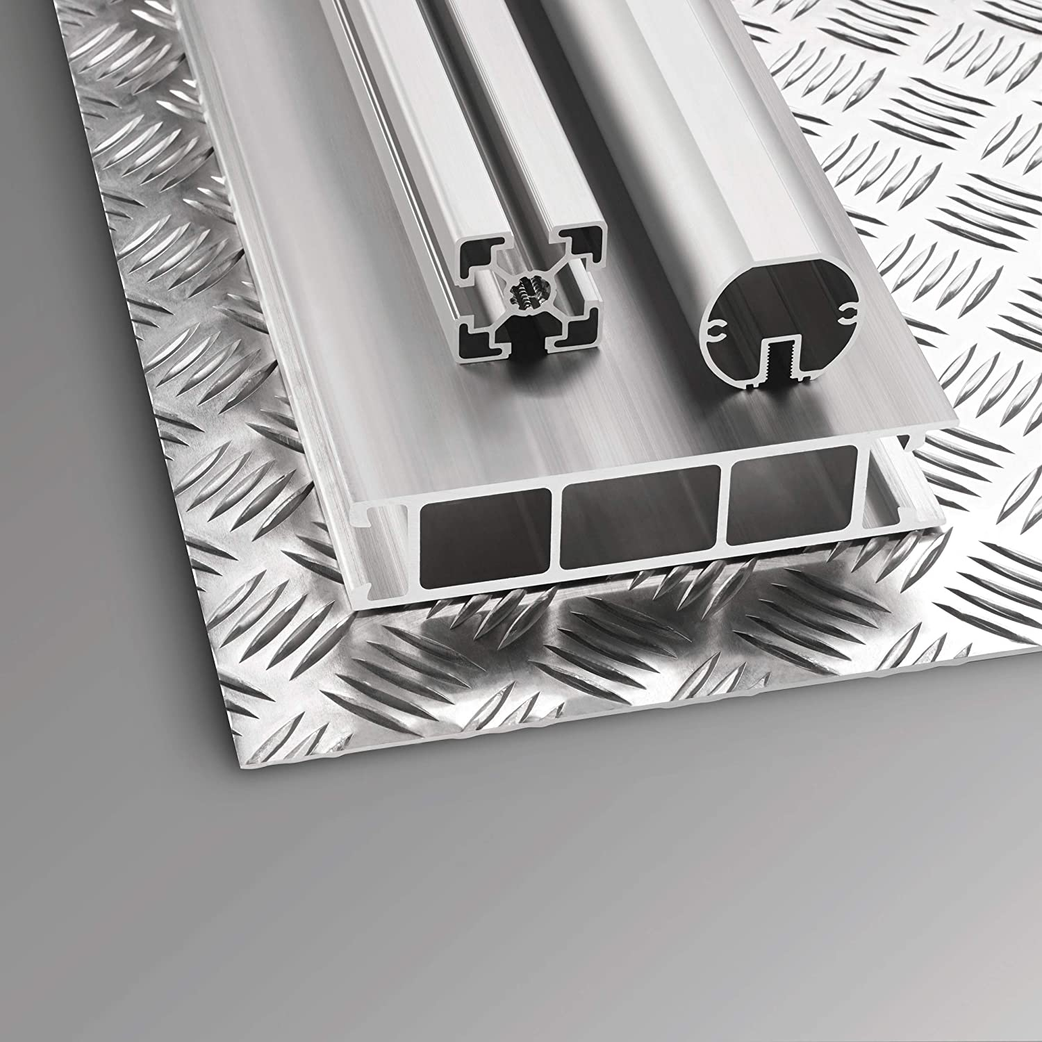 Aluminiumbleche und Metallprofile auf grauer Oberfläche, verschiedene Formen und Texturen zeigend.