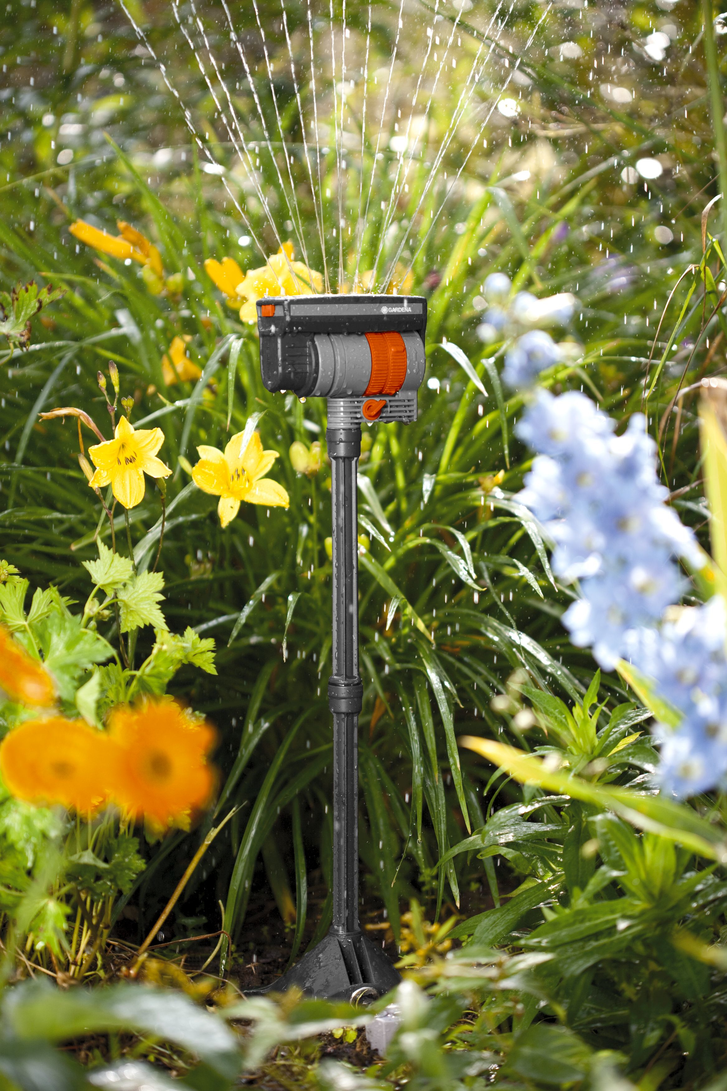 Een sproeier in een tuin. Water sproeit in de lucht, omringd door planten en bloemen.