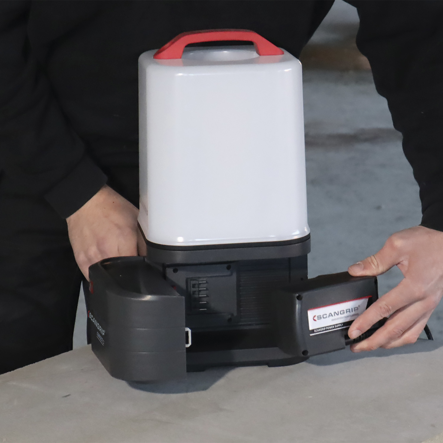 Eine Person öffnet das Batteriefach einer weiß-grauen Laterne. Der Markenname ist sichtbar.