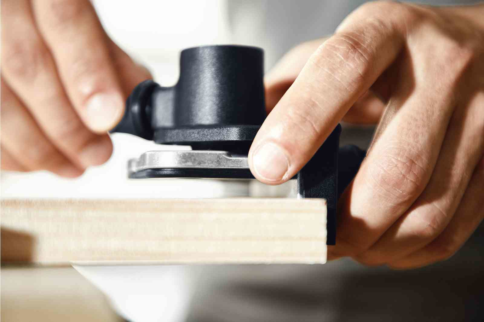 Dłonie trzymają narzędzie, blisko kawałka drewna. Narzędzie jest czarne.