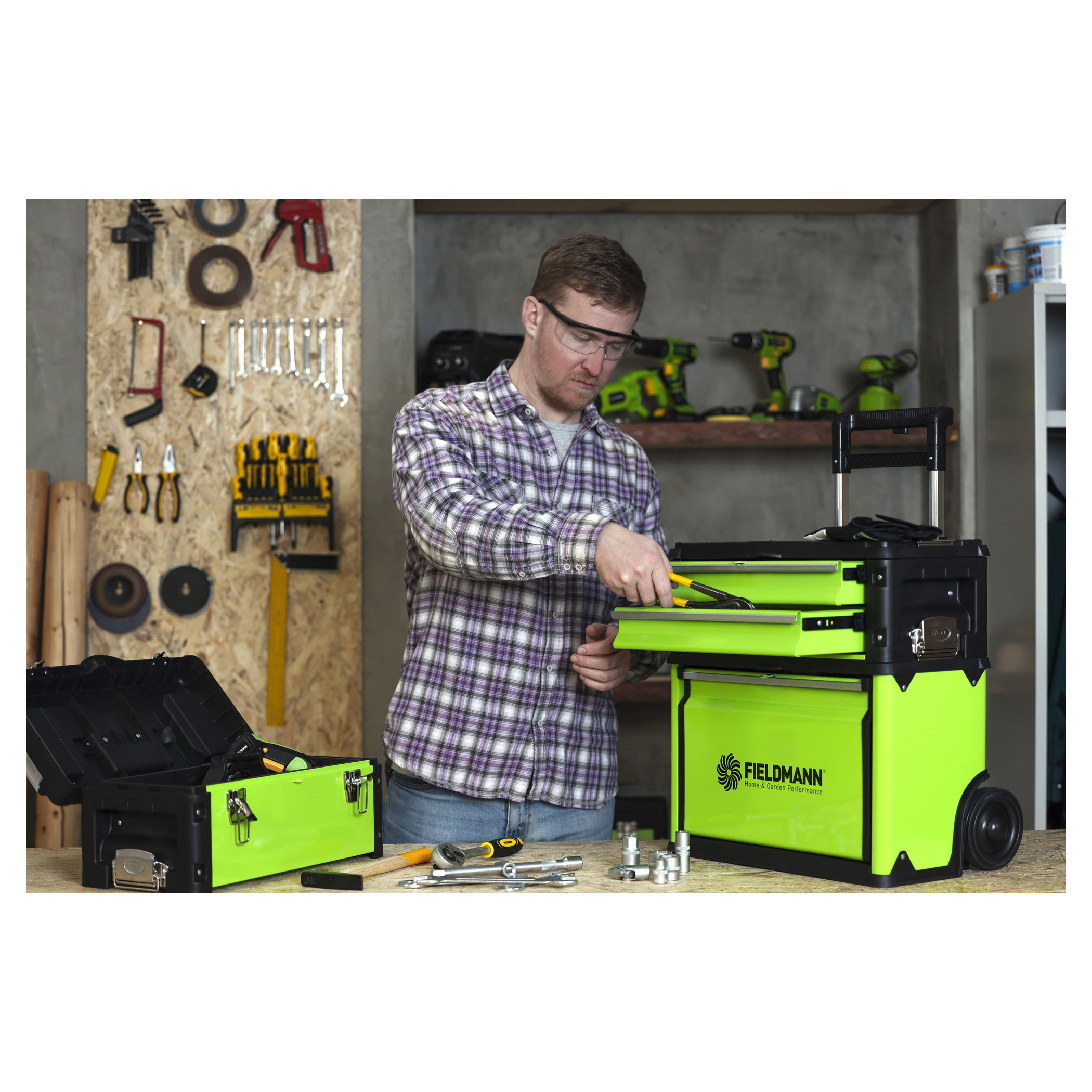 Mężczyzna w koszuli w kratę używa zielonej skrzynki narzędziowej. Narzędzia na stole. Tło warsztatu.