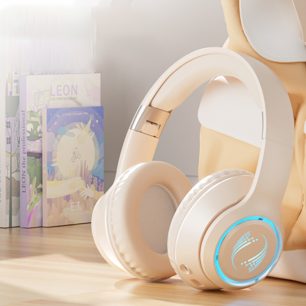Beige kabellose Kopfhörer mit blauen Lichtakzenten, die in der Nähe von Büchern und einer hellgelben Tasche liegen.
